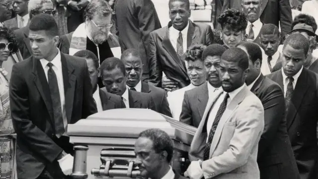 برادر کوچکتر بایس، جی پشت تابوت لن اشک می‌ریخت. او در دسامبر ۱۹۹۰ در یک حادثه تیراندازی کشته شد