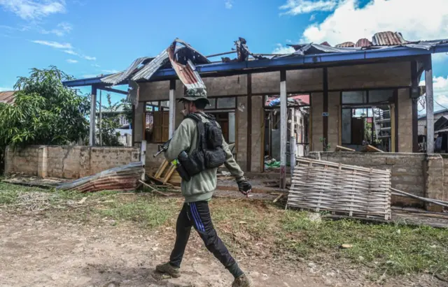 MOBYAE, SHAN STATE, MYANMAR - 2022/09/15: A People's Defence Force soldier walking in front of a house destroyed by the Burmese military air craft in Mobyae, Kayah State.