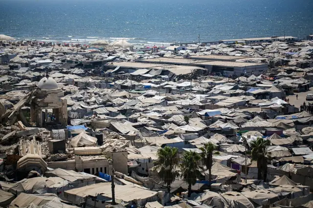 صورة عامة من الأعلى لخيام نازحين في مدينة غزة، التقطت نهاراً وأمام الخيام يمتد البحر ذو الموج الهادئ.