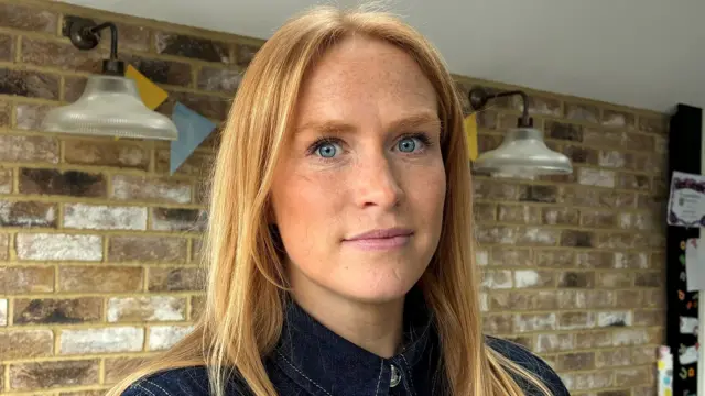 žena svetle kose stoji u prostoriji sa zidom od cigala