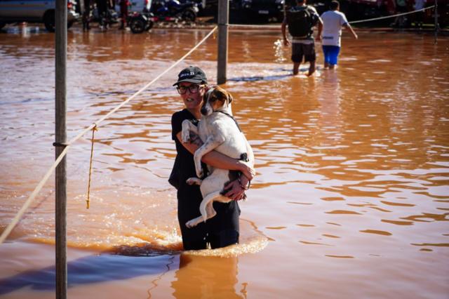 Mulher segurando cachorro no colo em meio  enchente