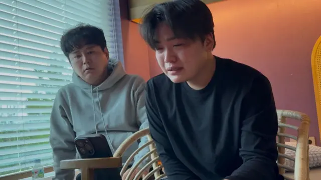 一张金城的照片；他是一名 21 岁、逃往首尔的朝鲜难民，刚得知母亲可能很快就会从中国监狱被遣返回朝鲜；他的养父坐在他身后。