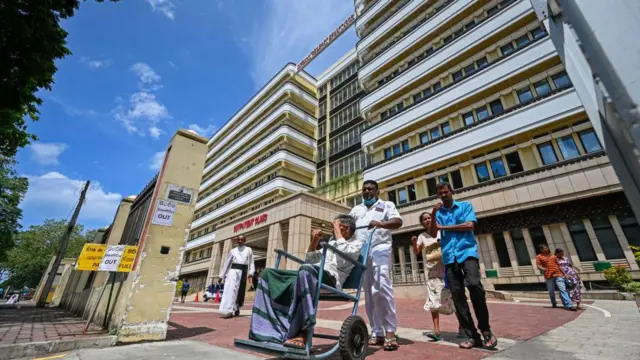 රෝගී පුද්ගලයෙකු රෝද පුටුවක තබාගෙන තල්ලු කරමින් යන අයුරු.