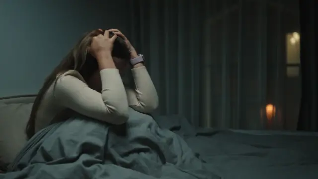 Mulher sentada na cama com a mão na cabeça na penumbra