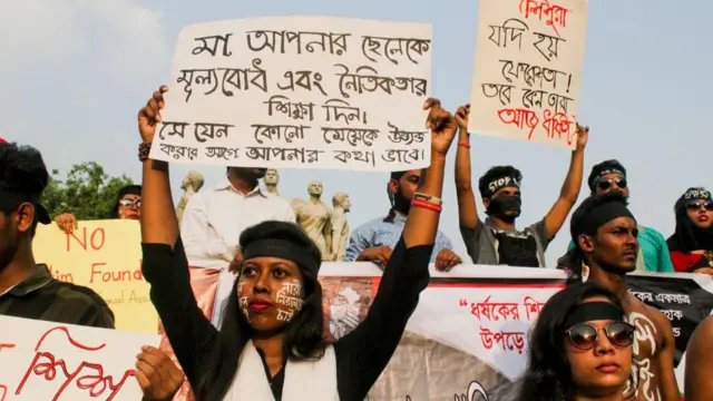 ধর্ষণবিরোধী এক বিক্ষোভ সমাবেশে ছেলে সন্তানকে নৈতিক শিক্ষা দেওয়ার জন্য প্ল্যাকার্ড ধরে রেখেছেন এক নারী 