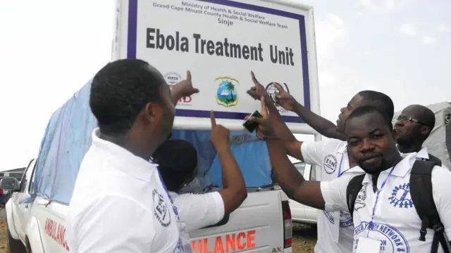 Patrick Faley (L) and other community workers in Sinje point to a sign saying 'Ebola Treatment Unit' during the outbreak in Liberia