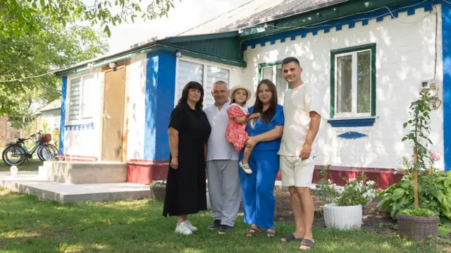 Людмила у колі родини - чоловіка, доньки, зятя та внучки. На фоні хати з рослинами, позаду видно велосипеди
