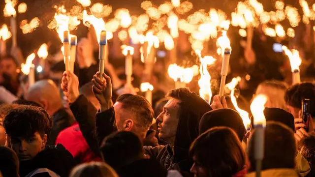 Учасники мітингу на підтримку партії опозиційного лідера перед виборами в Угорщині - люди стоять ввечері з факелами, їхні обличчя підсвічуюються