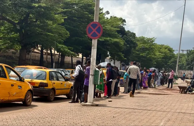 De nombreux taxis jaunes dans la circulation et plusieurs usagers debout sur le bord de route.