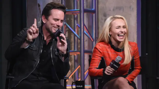 Hayden Panettiere sentada ao lado de Charles Esten, ambos segurando microfones em uma sessão de perguntas e respostas e rindo bastante.