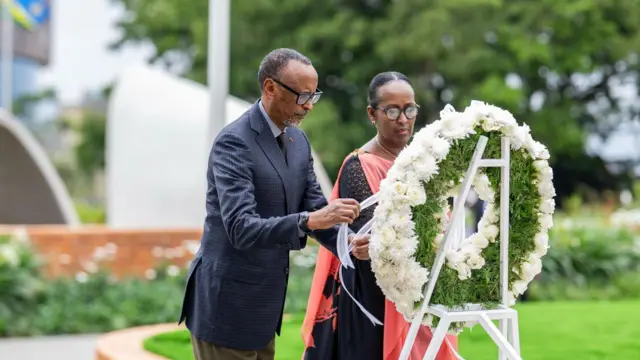 Perezida w'u Rwanda Paul Kagame n'umugore we Jeannette Kagame bashyira indabo ahashyinguwe intwari z'igihugu, i Kigali, mu Rwanda, ku cyumweru, ku itariki ya mbere Gashyantare (2) mu mwaka wa 2026. Kagame yambaye indorerwamo, ikositimu yijimye ijya kuba ubururu n'ipantalo y'ikigina ijya kuba khaki. Jeannette Kagame yambaye indorerwamo, n'ikanzu y'umukara n'umukenyero utukura ujya kweruruka. Inyuma yabo hari urukuta rw'amatafari ahiye rutaboneka neza, n'ibendera ry'u Rwanda n'ibiti bitaboneka neza.