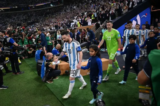 L'attaquant argentin Lionel Messi (numéro 10), et le gardien de but argentin Emiliano Martinez font leur entrée sur la pelouse du Lusail Stadium, le 18 décembre 2022, pour la finale de la Coupe du monde de football Qatar 2022 opposant l'Argentine à la France. 
