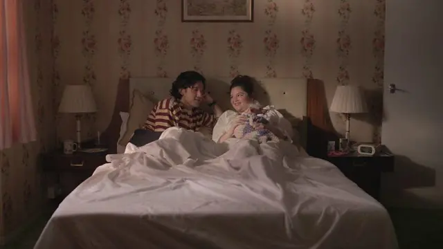 Casal deitado na cama em cena de "Too Much"
