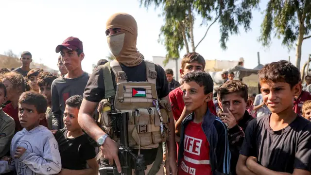 Un miliciano enmascarado de las Brigadas Ezzedine al-Qassam, el brazo armado de Hamás, hace guardia armado con un fusil rodeado de niños en el sur de Deir el-Balah, en el centro de la franja de Gaza, poco antes de la entrega de rehenes israelíes. 