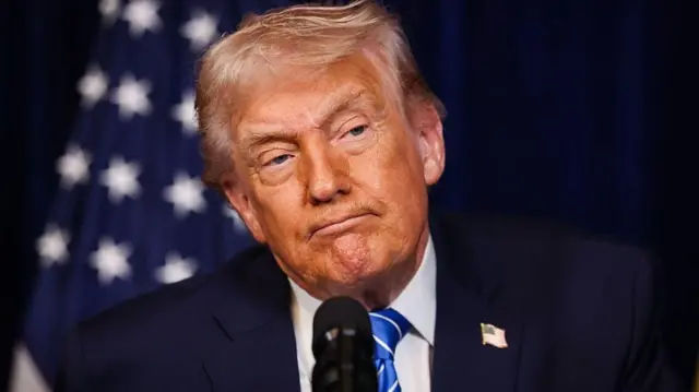 12月28日のトランプ氏の胸から上のアップ写真。口を結んで少し頭を傾けて前を見ている。背後に米国旗がぼんやり写っている