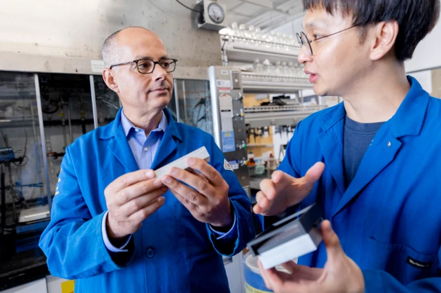 Omar Yaghi con una bata azul habla con un estudiante también con una bata azul