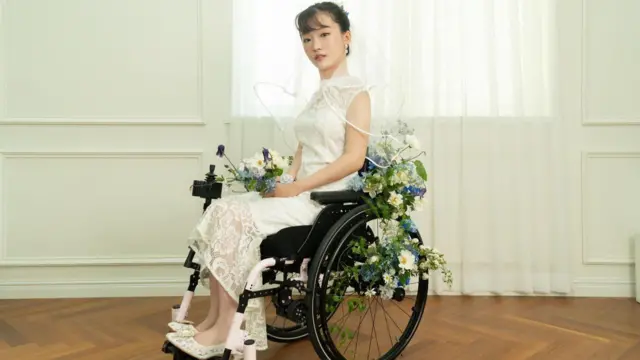 یوه کوریایۍ ښځه په ویلچېیر کې ناسته ده چې د واده جامې یې اغوستې دي. ګرځنده څوکۍ يې پر ګلانو ښکلې شوې ده.