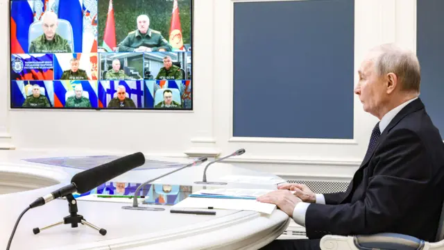 Владимир Путин и экран, на котором видно российское военное руководство и белорусский лидер Александр Лукашенко