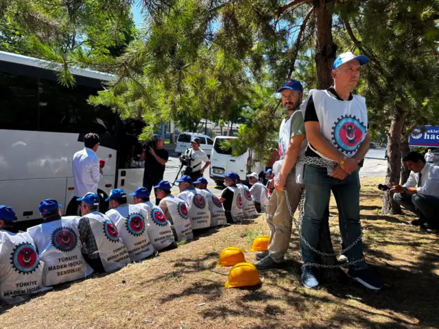 Türkiye Maden İşçileri Sendikası işçileri kendilerini ağaçlar zincirlemiş. Arkada tek sıra halinde oturan işçiler var