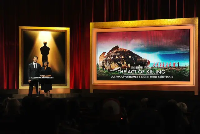 Chris Hemsworth dan Presiden Academy Cheryl Boone Isaacs mengumumkan 'The Act of Killing' sebagai nominasi Film Dokumenter Terbaik pada Pengumuman Nominasi Academy Awards ke-86 di Teater Samuel Goldwyn AMPAS pada 16 Januari 2014 di Beverly Hills, California.