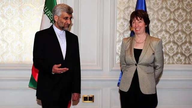 سعید جلیلی با پیراهن سفید و کت و شلوار سیاه با عینک در کنار کاترین اشتون با کت طلایی و دامن سیاه