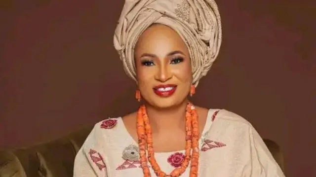 Halimat Adenike Tejuosho wọ aṣọ òfì, wọ ilẹ̀kẹ̀ sọ́rùn, ò ǹ rẹ́rìn-ín sí ẹ̀rọ ayàwòrán