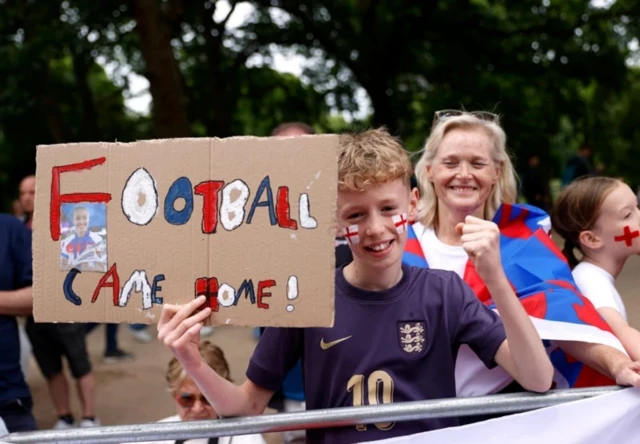 Мальчик держит картонку с надписью «футбол вернулся домой»