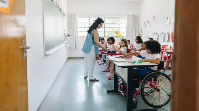 Foto de uma sala de aula com uma criança em uma cadeira de rodas. 