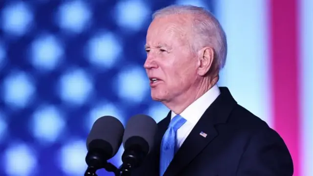 Joe Biden discursando, com bandeira dos EUAno funciona bwintelão ao fundo