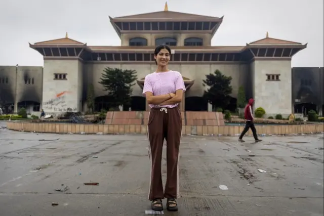 devojka stoji ispred zapaljene zgrade parlamenta u Nepalu