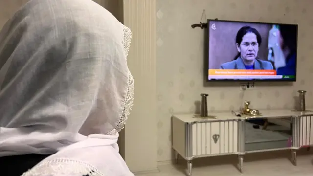 Bir kadın arkadan görünüyor. Televizyon seyrediyor.