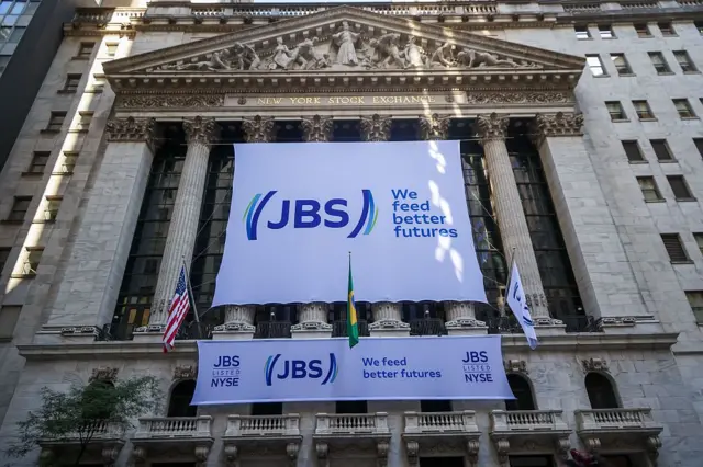 Dos grandes letreros blancos con el logo de JBS y el lema "Alimentamos mejores futuros" escritos en blanco, en la fachada del edificio de la Bolsa de Nueva York