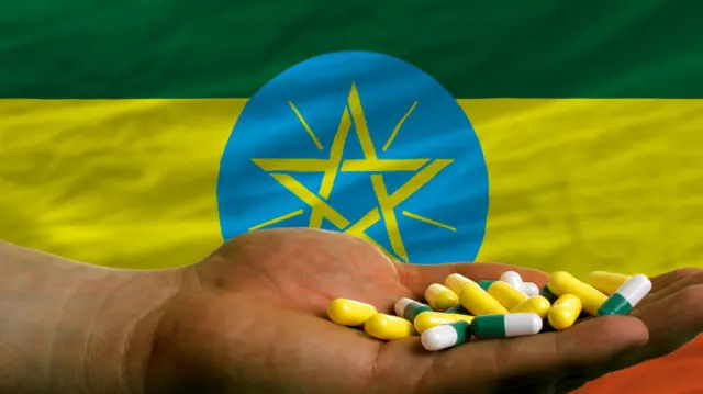 መድሃኒት በእጁ የያዘ ሰው ከኢትዮጵያ ባንዲራ ፊት ለፊት