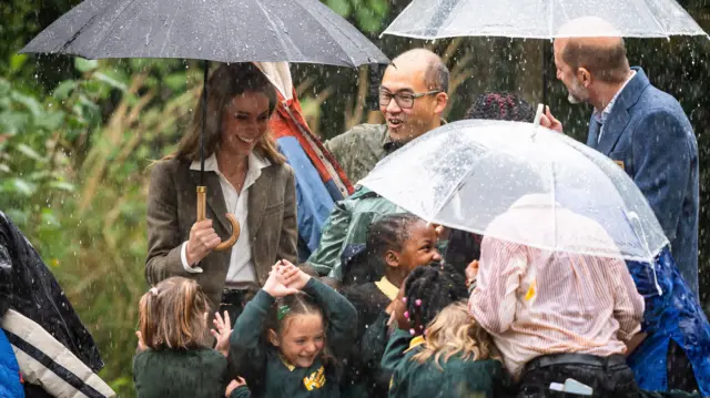 Четыре взрослых, включая Кэтрин, которая держит один из трех зонтов, и пять молодых школьников.