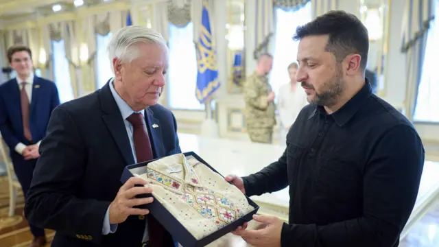 Линдзи Грејем у оделу држи поклон Владимира Зеленског - традиционалну везену кошуљу