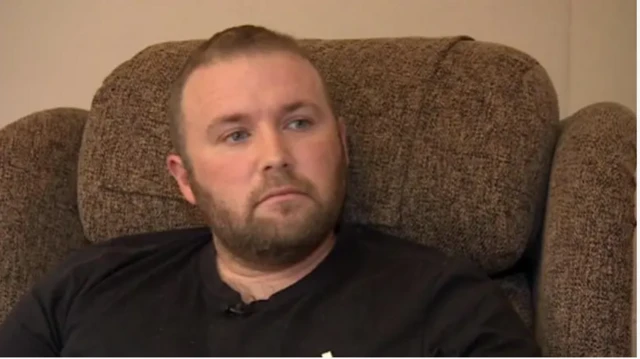 Man sat on sofa looking to the side and wearing a black t shirt