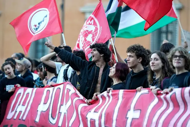 Filistin bayrakları taşıyan siyah giyimli gençler, biri elini kaldırmış, bağırıyor.