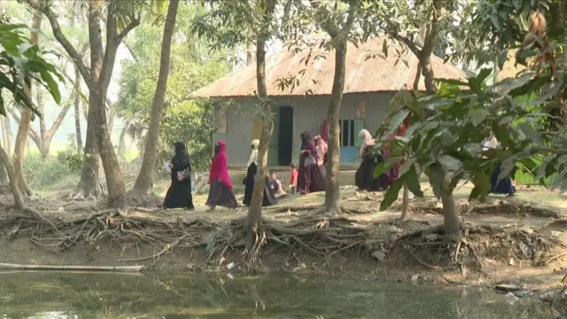 একটি পুকুরের পাড়ে গাছাপালা ঘেরা রাস্তা ধরে হেঁটে যাচ্ছেন বোরকা পরা কয়েকজন নারী