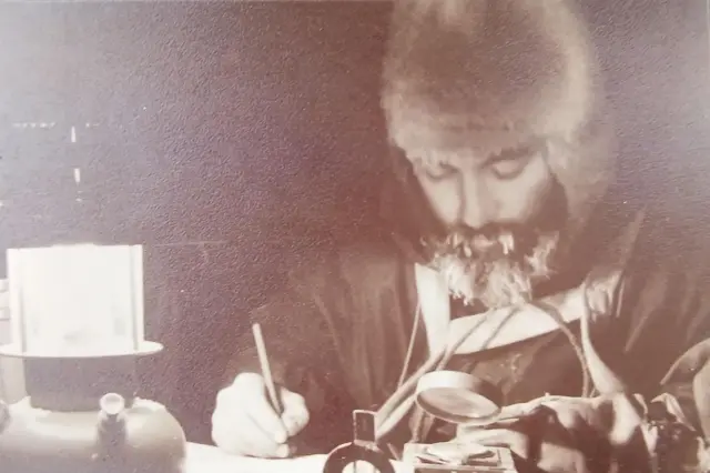 Uma foto em sépia de um homem escrevendo algo e segurando uma lupa