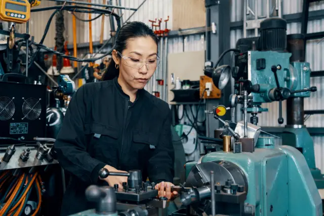 جاپان کې یوه ښځه د فلزي توکو جوړولو په کارځای کې ماشیني تجهیزات کاروي. 