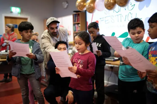 بهائيون وضيوف من ديانات أخرى يشاهدون مجموعة من الأطفال وهم يؤدون مسرحية في مركز إيدا كينسي في مانشستر بإنجلترا للاحتفال بعيد النوروز الذي يمثل الاعتدال الربيعي وبداية السنة البهائية الجديدة، صورة تعود لـ 20 مارس 2024