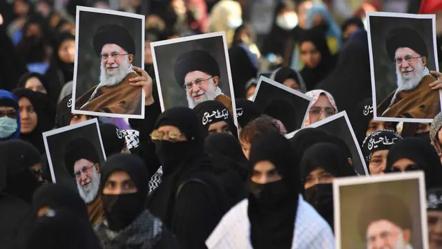 Iranianos em rua levando fotografias do aiatolá nas mãos.
