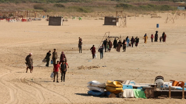 Moradores carregando seus pertences por uma praia, ao deixar a cidade litorânea de Tiro.