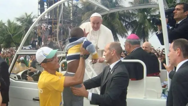 Foto de Rennan Laurente segurando uma criança enquanto o papa Francisco o abençoa nas ruas de Copacabana. 