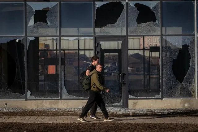 Мужчины идут мимо здания с выбитыми в результате обстрела окнами в Белгороде