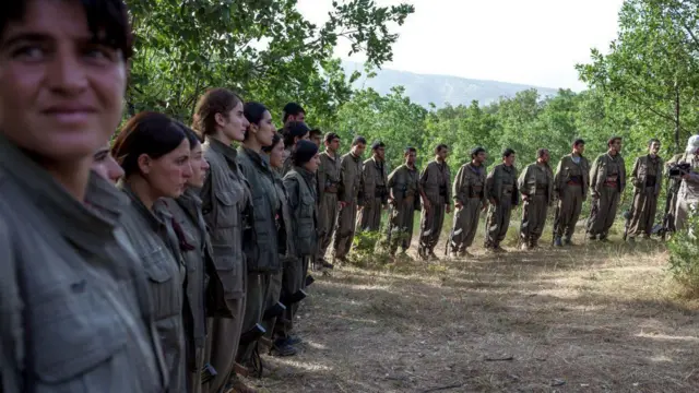 Yan yana sıralanmış kadın savaşçılar, kırsalda ayakta duruyor.