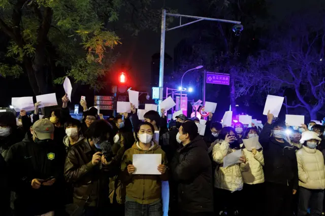 People hold white sheets of paper in protest over coronavirus disease (COVID-19) restrictions after a vigil for the victims of a fire in Urumqi, as outbreaks of COVID-19 continue, in Beijing,