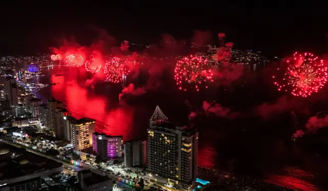 Una explosión de fuegos artificiales rojos iluminan la bahía de Acapulco