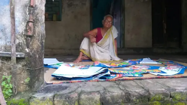 বাড়ির দাওয়ায় বসে কাজ করছেন রেবা পাল। 