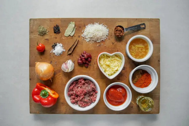 Vue plongeante sur les ingrédients bruts d'un Chilli con Carne sur une planche à découper en bois.